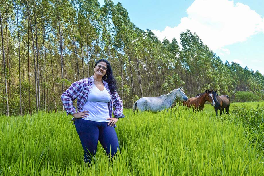 Produtora rural sorrindo em frente ao plantio de eucalipto e cavalos